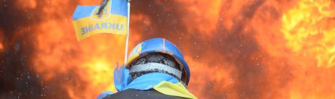 Protester wearing Ukraine state flag colors facing the massive fire set by protesters to prevent internal forces from crossing the barricade line Source: Wikimedia